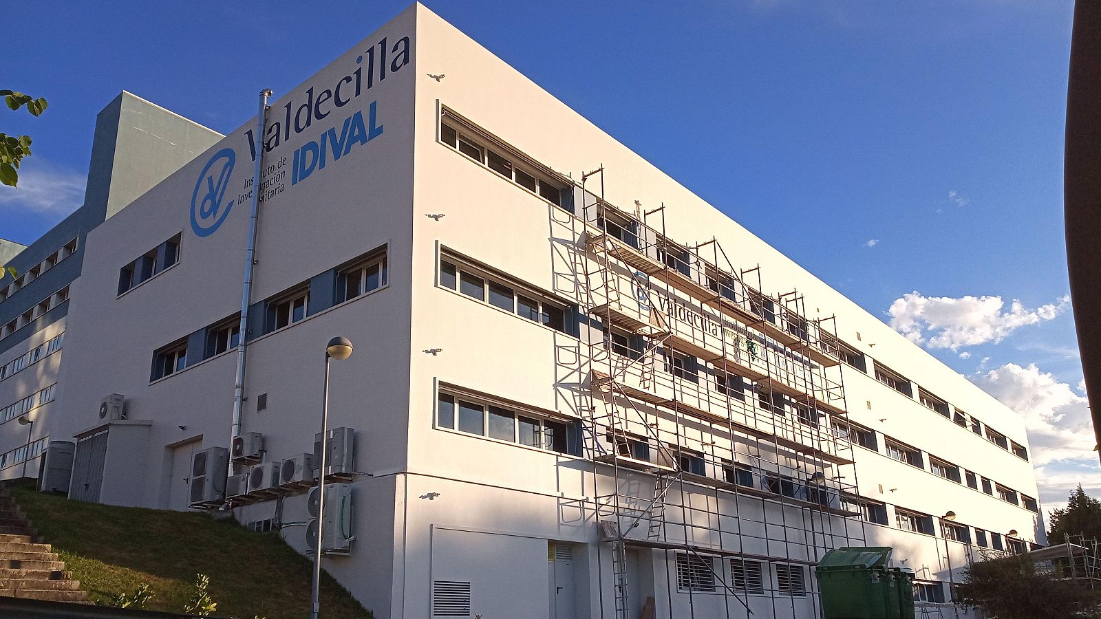 Fachada de hospital con andamios, varios pisos y ventanas.  Se ven aparatos de aire acondicionado y el nombre "Valdecilla" con el logo "IDIVAL" en la parte superior.
