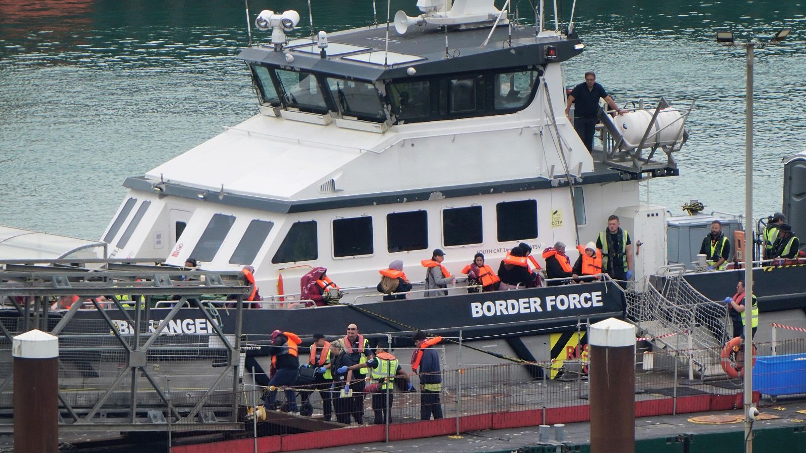 Desembarco de personas con chalecos salvavidas naranjas de un barco de la Border Force, asistidas por personal uniformado en el muelle.