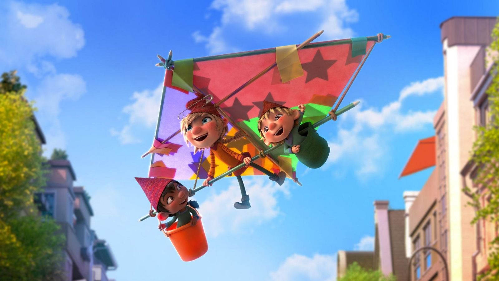 Tres Elfkins disfrutan de un vuelo en una cometa casera de vivos colores sobre una ciudad. Uno lleva jersey naranja, otro camisa verde y el tercero, un gorro rojo, viaja en un cubo.