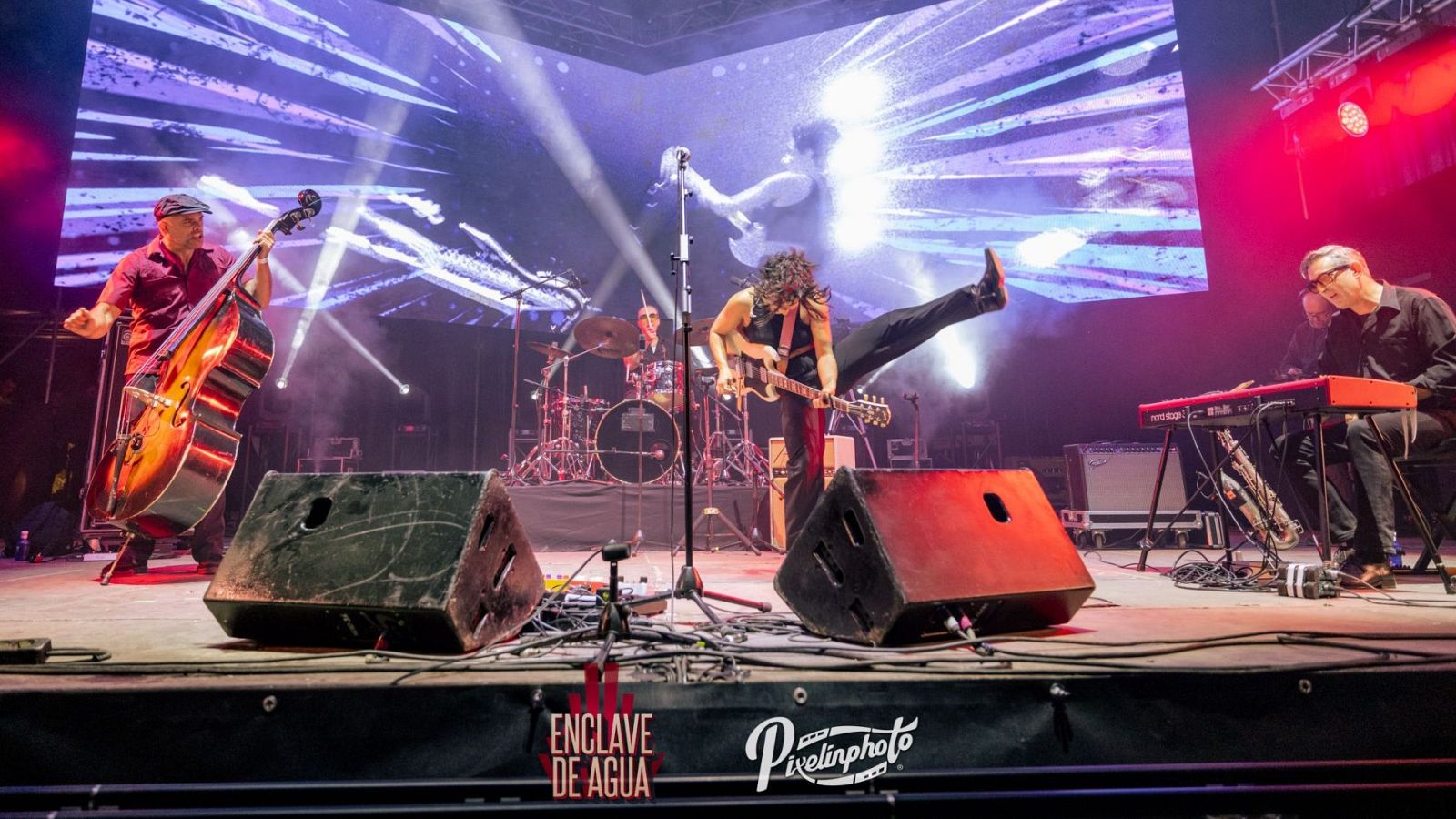 Concierto en directo de una banda de cuatro músicos (bajo, guitarra, batería, teclado) con una pantalla de fondo y logo de Radio 3.  Se aprecia gran energía en la actuación.