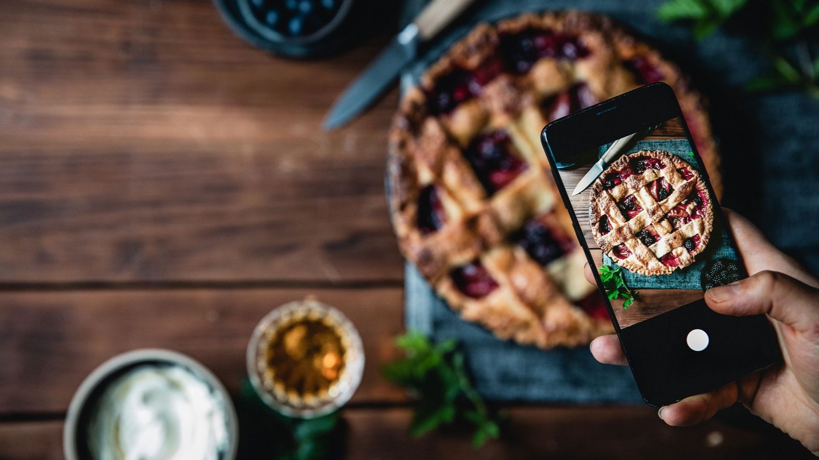 Tarta de frutos rojos fotografiada con un móvil.  Menta, arándanos y nata adornan la escena, lista para ser compartida online.