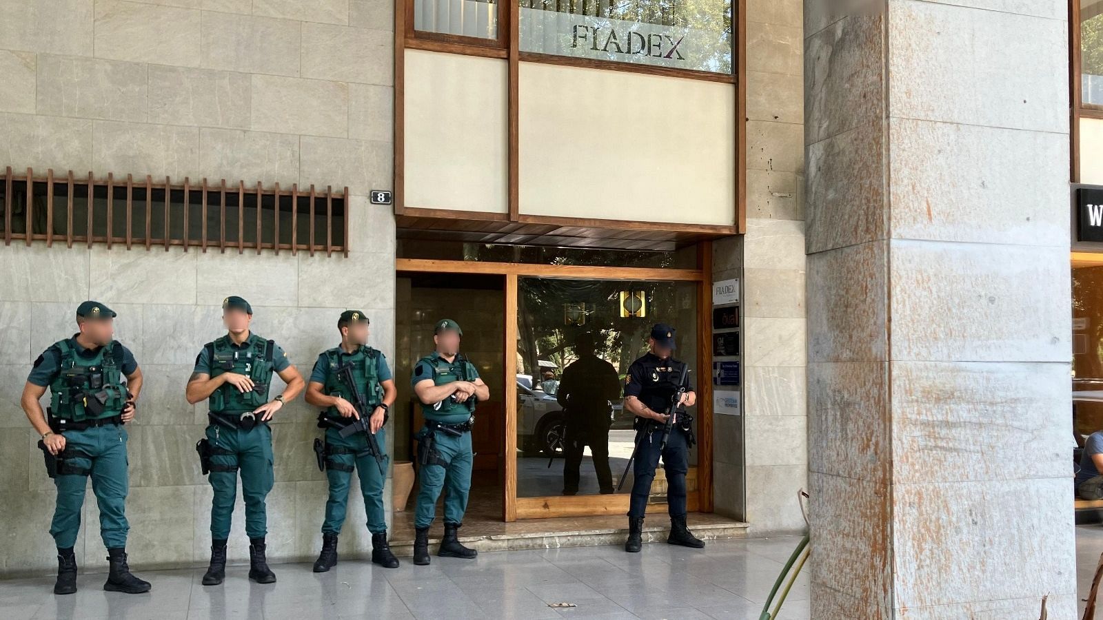 Agentes de la Guardia Civil, algunos en uniforme verde, otros de negro, frente a un edificio 'FIADEX' con el número 8.  Posible escena de una operación policial.