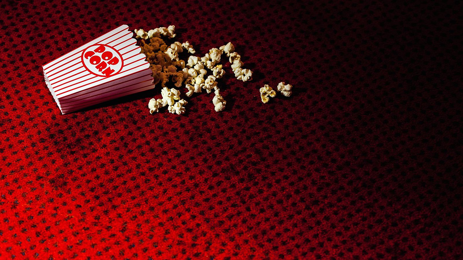 Palomitas de maíz esparcidas alrededor de un envase de cartón rojo y blanco con la palabra "Popcorn".