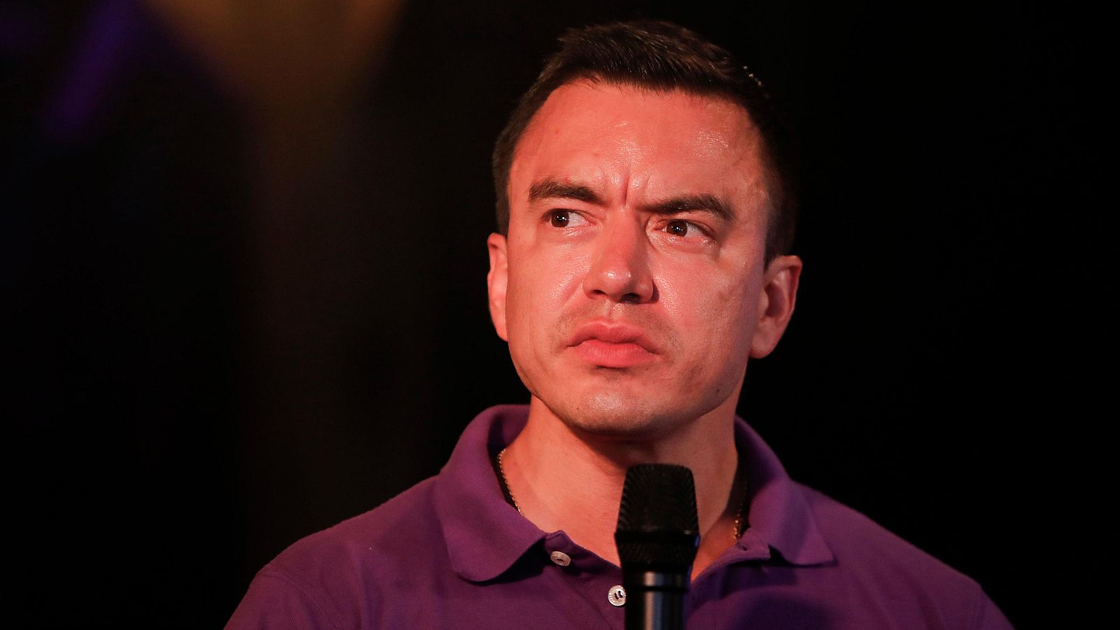 Daniel Noboa, con camisa morada, ofrece declaraciones tras conocer los resultados electorales.  Su expresión es seria, frente a un micrófono con fondo oscuro.