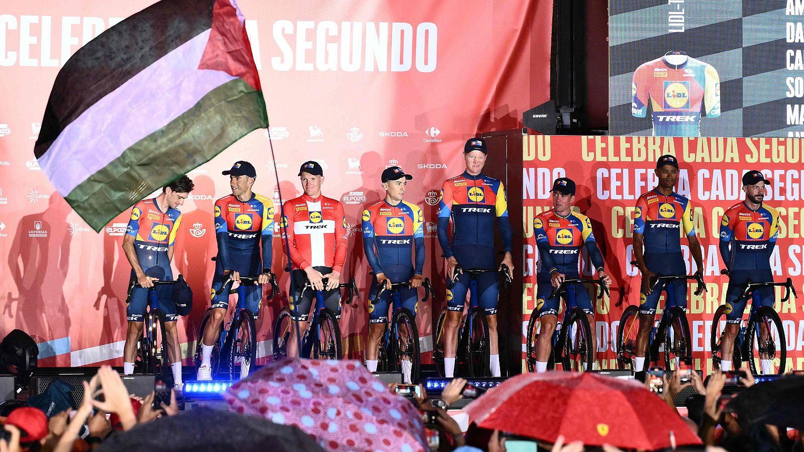 Una bandera palestina es ondeada en el acto de presentación de equipos de la Vuelta 2025 en Turín, con los corredores del Lidl en el escenario