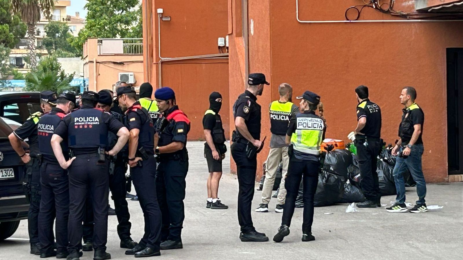 Confiscación de mercancía en operación anti-top manta. Varios agentes de diferentes cuerpos policiales, algunos con chalecos reflectantes, junto a bolsas de basura.