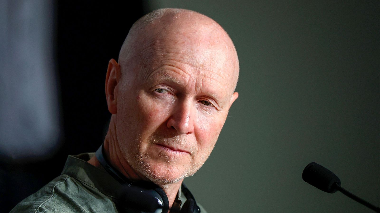 Paul Laverty, guionista, en primer plano durante una entrevista.  Expresión seria, camisa verde oliva y auriculares.  Ambiente interior.