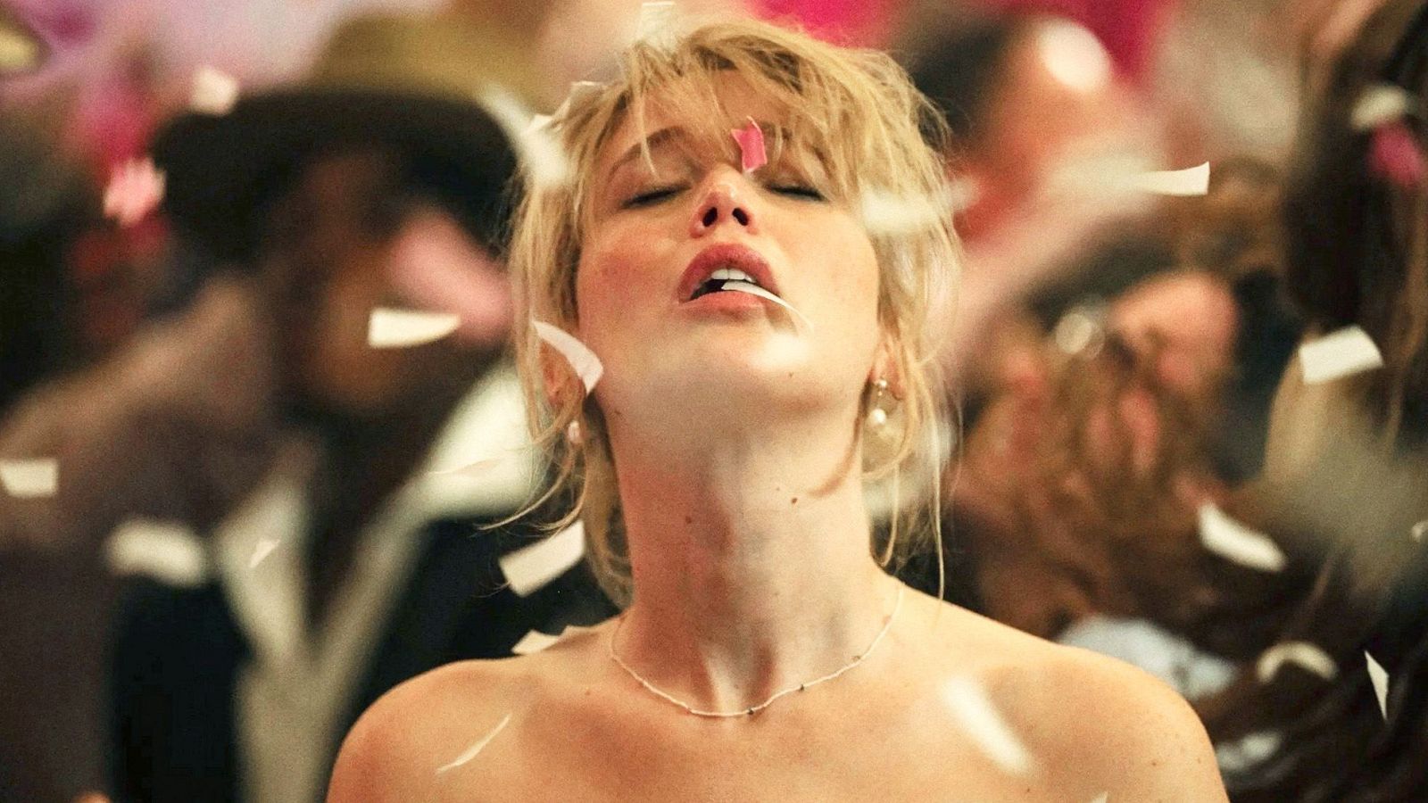 Actriz con confeti en el rostro, cabello suelto y expresión de alegría en un evento multitudinario.