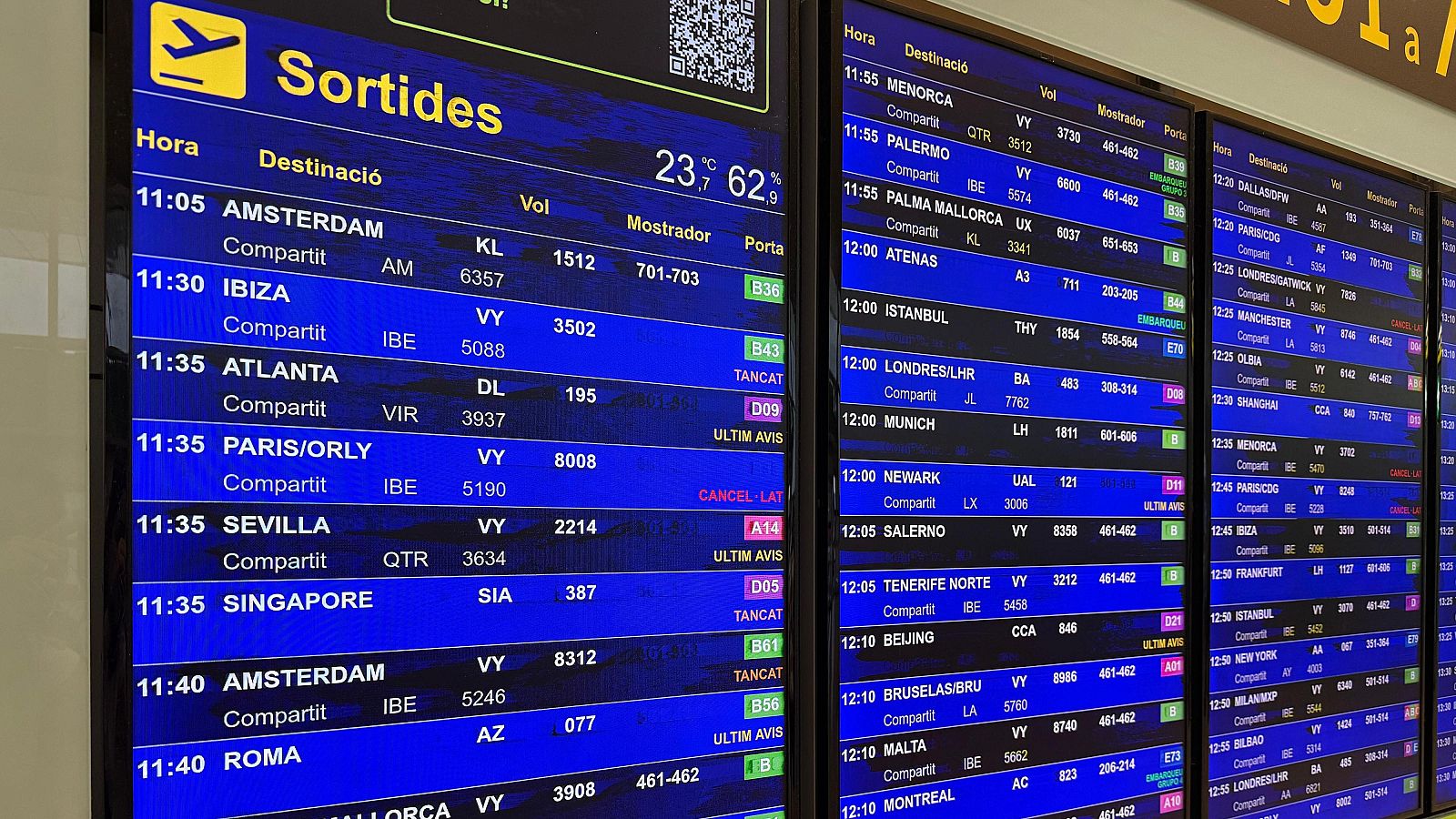 Panel de salidas de vuelos con información de hora, destino, estado (abierto, cerrado, cancelado) y puerta de embarque, en catalán e inglés.  Se muestran numerosos destinos.