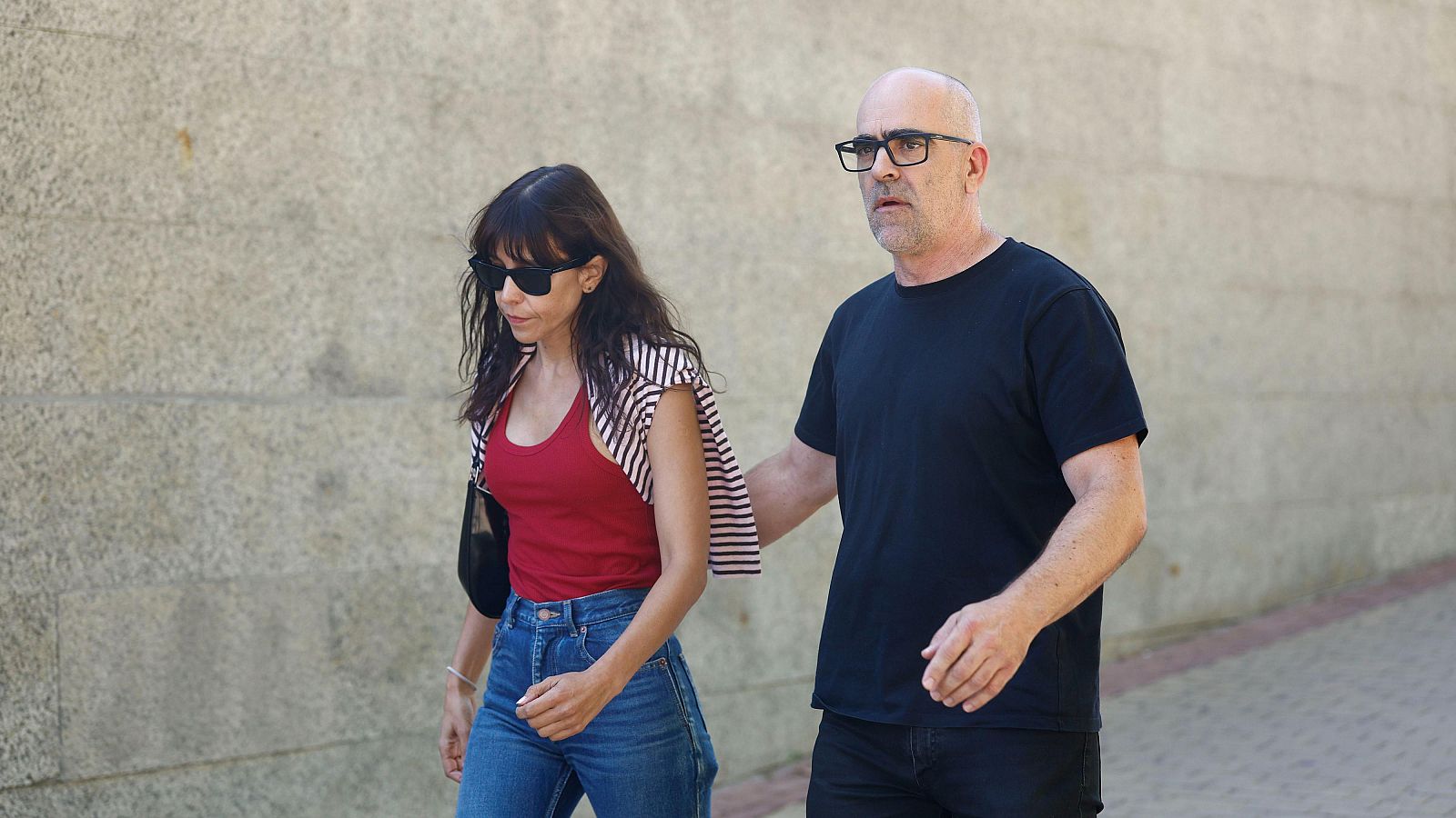 Luis Tosar y una mujer caminan juntos, él con camiseta negra y ella con camiseta roja y camisa a rayas, hacia una capilla ardiente. Foto: EFE/Rodrigo Jiménez.