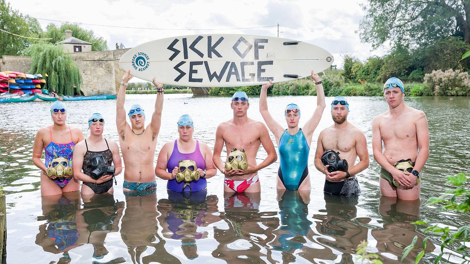 Los ocho nadadores británicos que participan en la acción 'Thames Swim Against Sewage' posan con una tabla de surf a modo de pancarta en la que protestan por la contaminación de los ríos