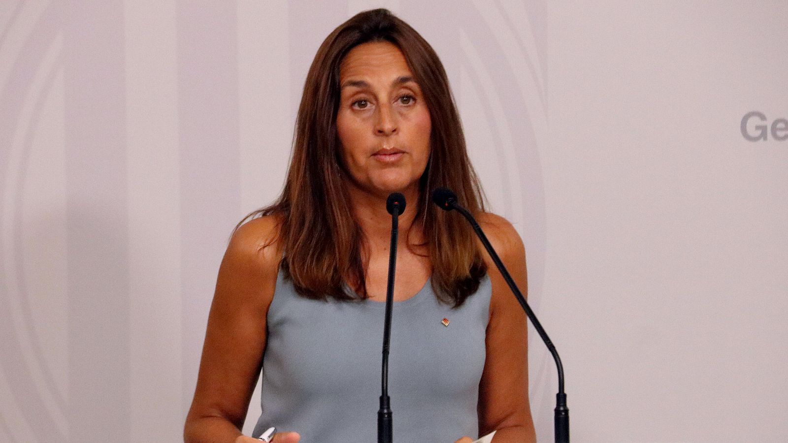 Consejera de Educación ante micrófonos, durante presentación del inicio de curso escolar.  Blusa gris azulada, cabello castaño liso. Fotografía de Guifré Jordan.