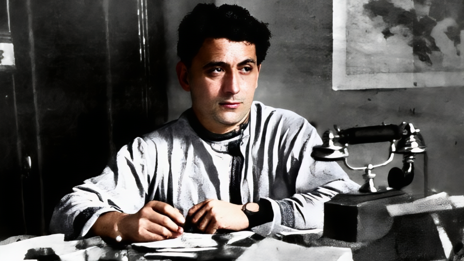 Andreu Nin, en blanco y negro, sentado a un escritorio escribiendo; lleva camisa de manga larga y reloj; teléfono antiguo sobre la mesa; fondo con mapa o imagen.