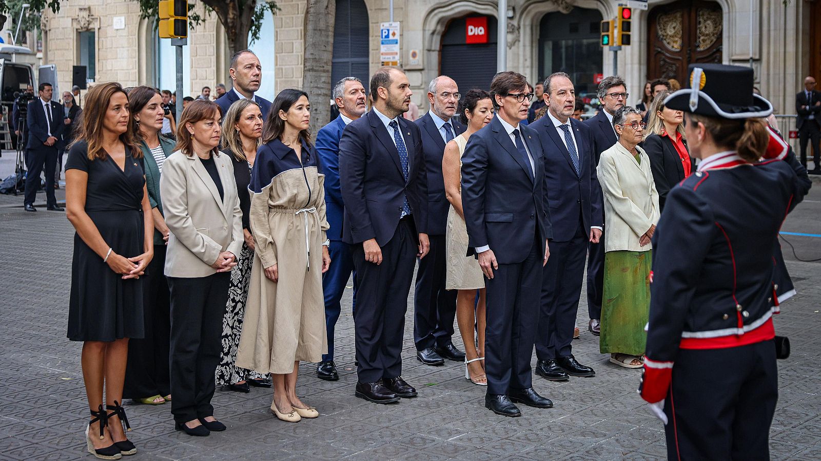 Ofrena floral del Govern a monument de Barcelona durant la Diada.  Salvador Illa presideix l'acte, amb membres del govern en vestimenta formal i un agent de seguretat present.