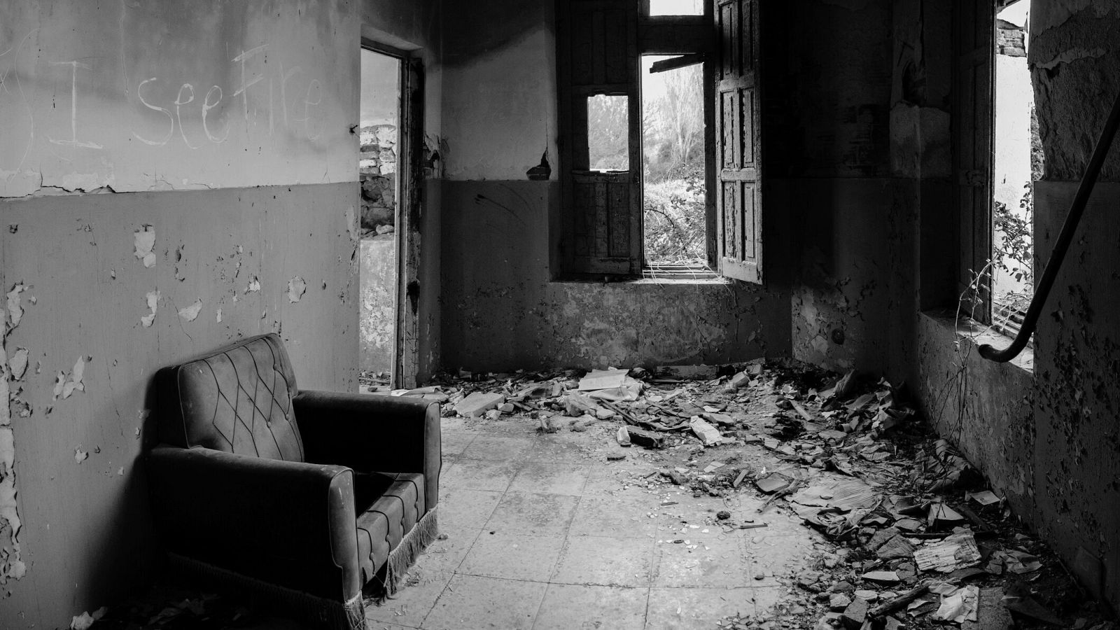 Ruinas de un edificio con un sofá antiguo, paredes descascarilladas, ventanas rotas y la frase "I see fire" escrita en una pared.  Imagen en blanco y negro.