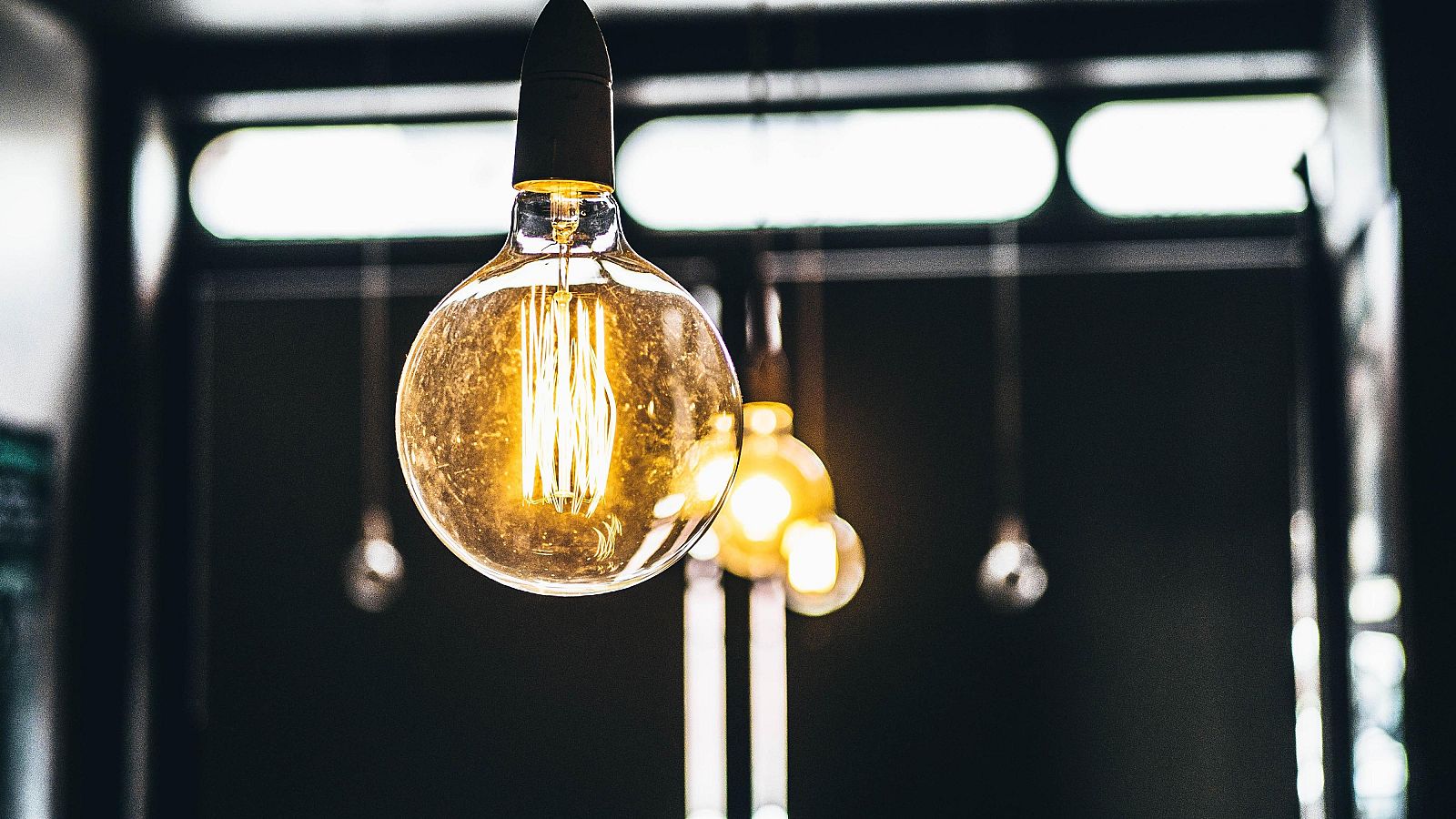 Bombilla incandescente vintage iluminada, con filamentos visibles, sobre fondo oscuro con otras bombillas desenfocadas.  Luz cálida y amarillenta.