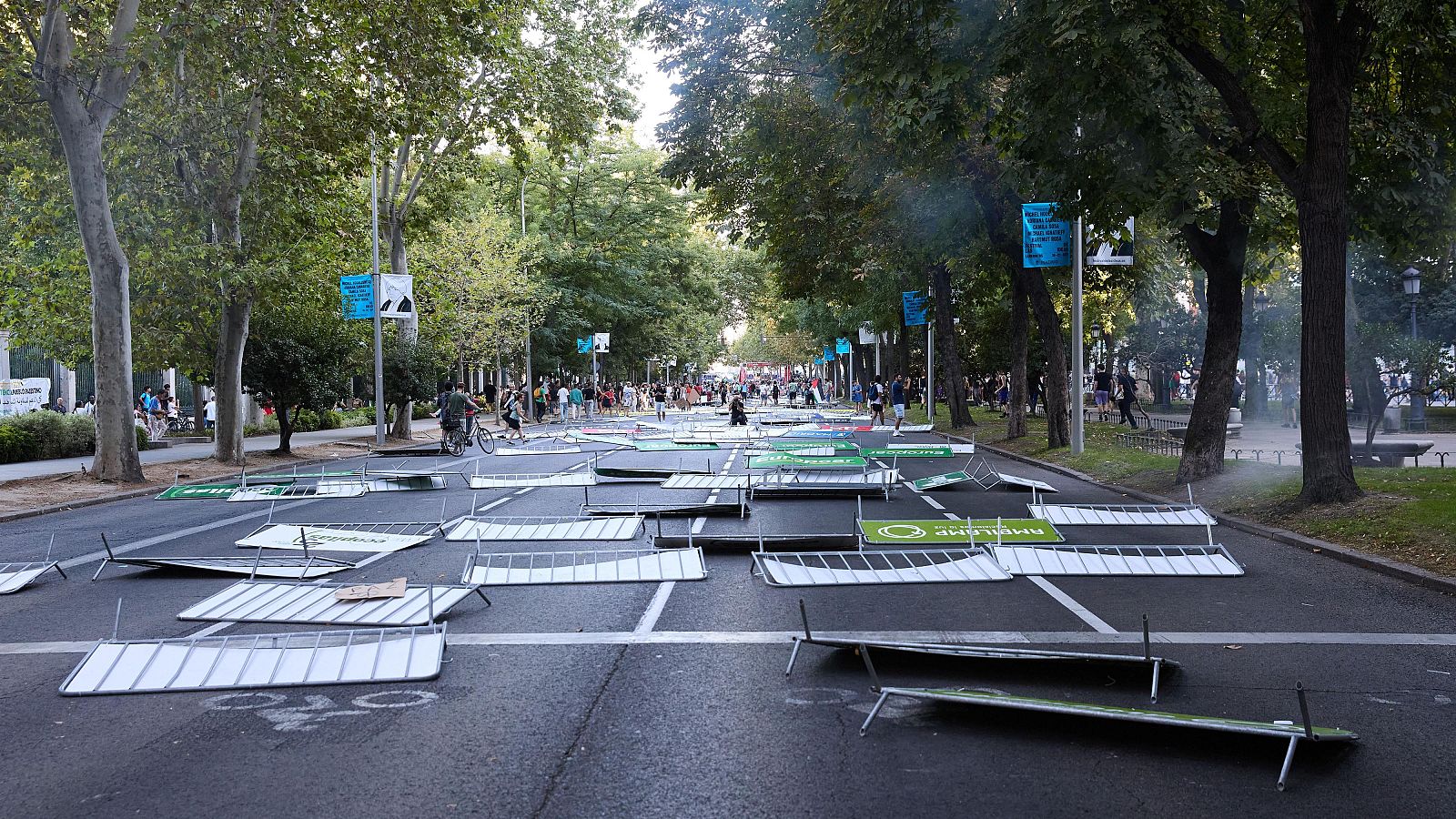 Vallas publicitarias metálicas derribadas tras una protesta.  Se observa humo o neblina y un grupo de personas al fondo.