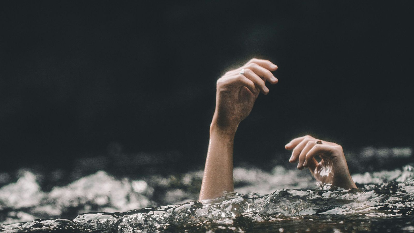 Manos emergiendo de agua oscura, dedos extendidos en señal de auxilio.  Imagen que refleja desesperación y peligro.