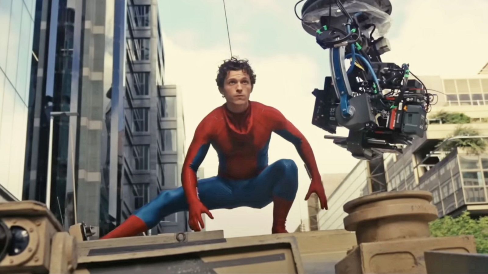 Spider-Man, en cuclillas sobre un vehículo, mira hacia adelante.  Escena de rodaje en ciudad, con cámara aérea.