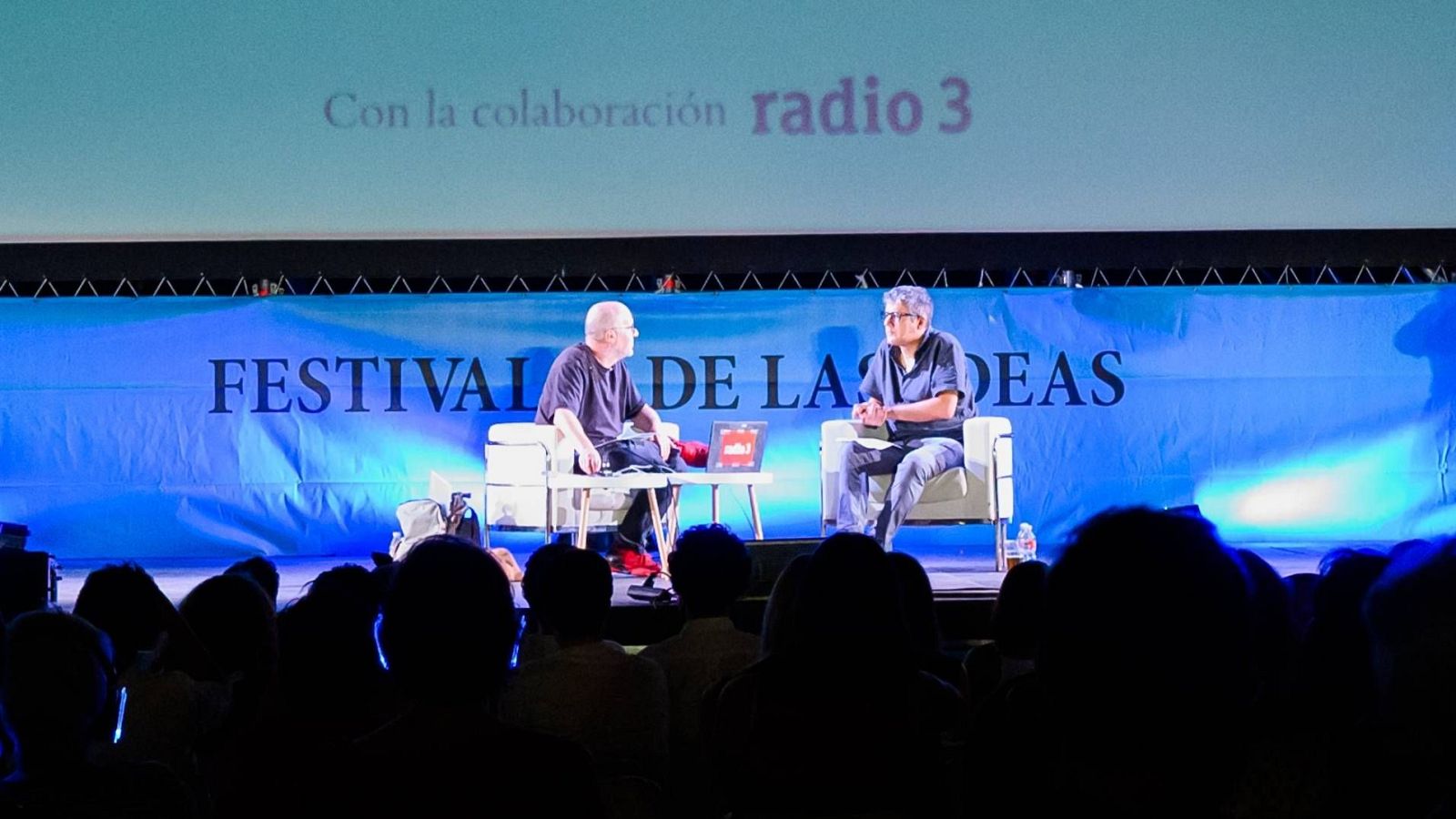 Conversación en el escenario de un festival, con un público presente. Se proyecta "Con la colaboración Radio 3".