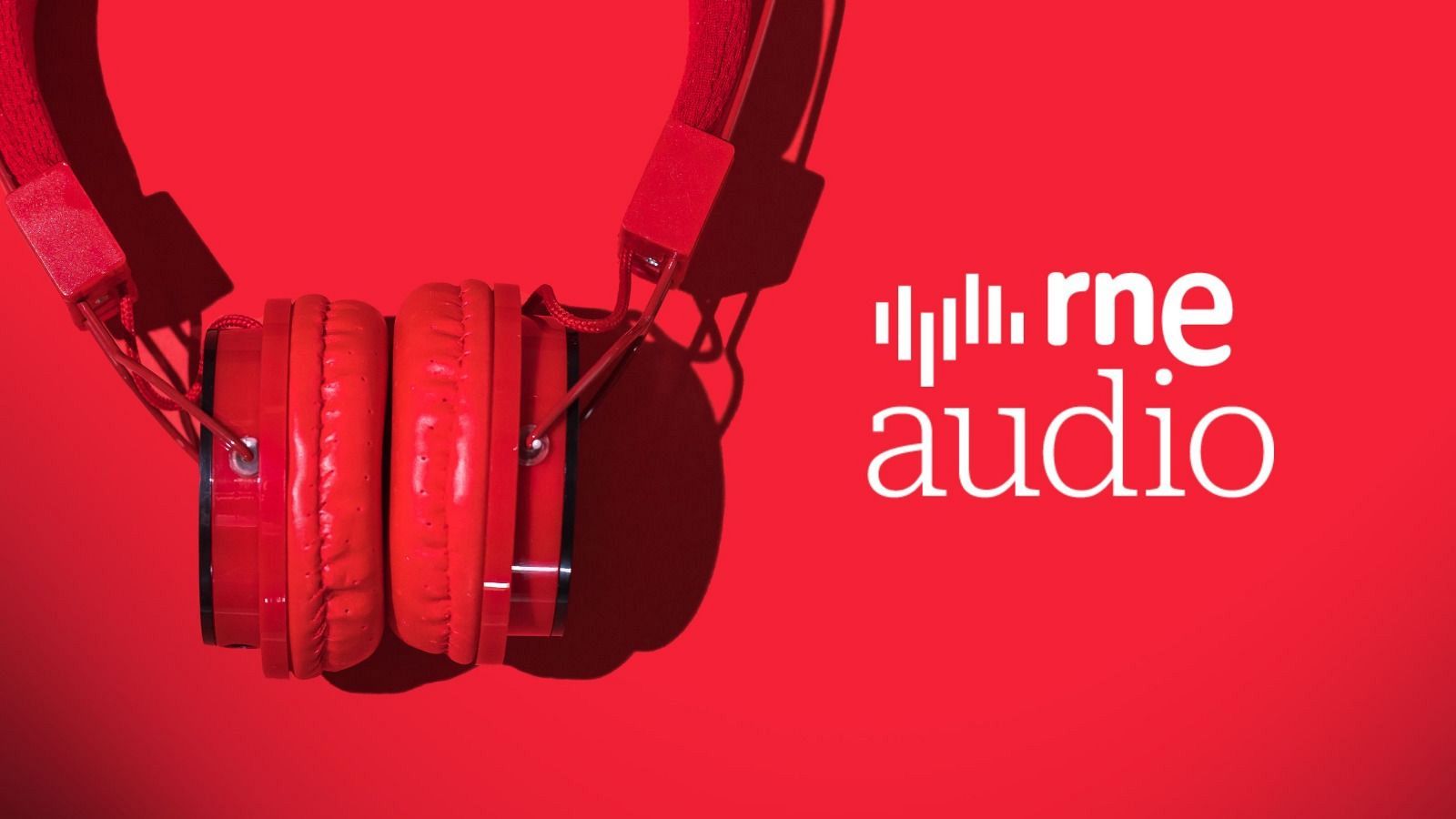 Unos auriculares rojos, con almohadillas acolchadas y el texto "rne audio" en blanco, cuelgan sobre un fondo rojo, posiblemente para escuchar contenido de audio.