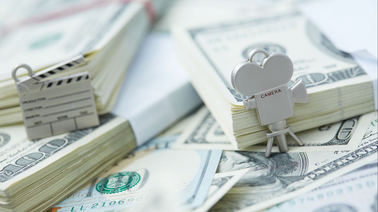 La imagen muestra billetes de dólares apilados, con una claqueta y una cámara de cine en miniatura, sugiriendo una relación entre la financiación y la producción cinematográfica.