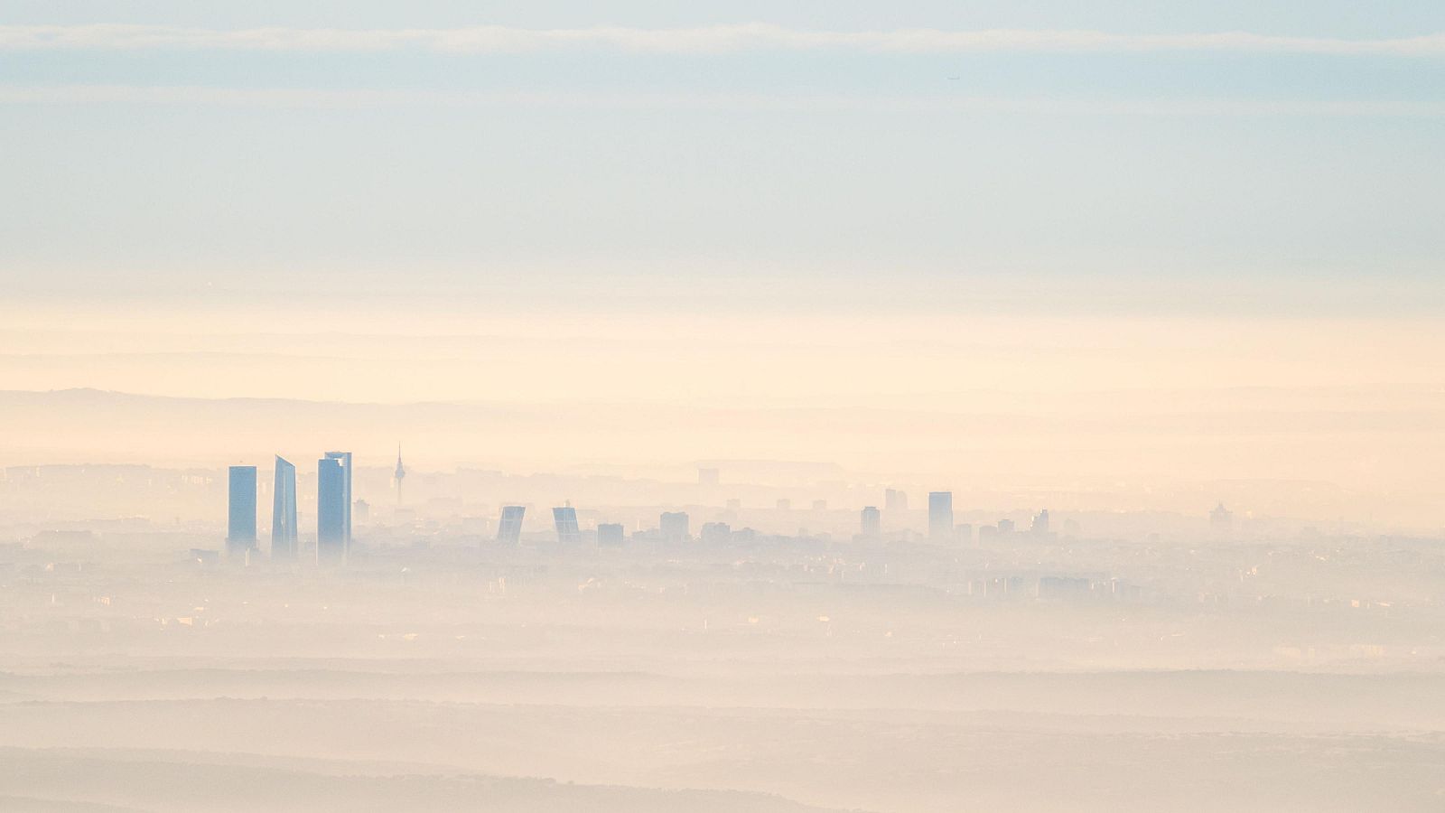 La imagen muestra una ciudad española cubierta por una densa capa de contaminación. Se distinguen algunos edificios altos entre la bruma, mientras que el resto del paisaje urbano se difumina, creando una atmósfera de poca visibilidad.