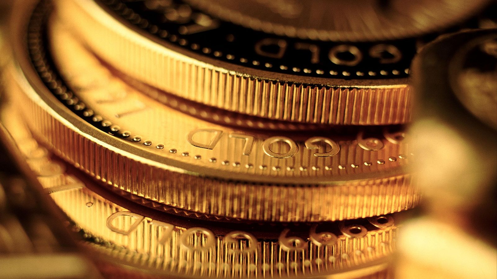 Primer plano de monedas doradas apiladas, con la palabra "GOLD" grabada. La imagen podría estar relacionada con la reciente caída del precio del oro, a pesar de mantenerse en máximos históricos.