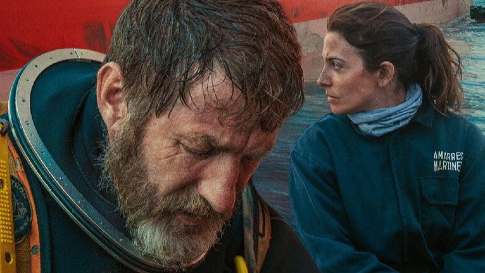 Antonio de la Torre, con traje de buzo, y Bárbara Lennie, con un mono azul con texto, posan juntos. Se encuentran en un entorno marítimo, con un barco visible al fondo.