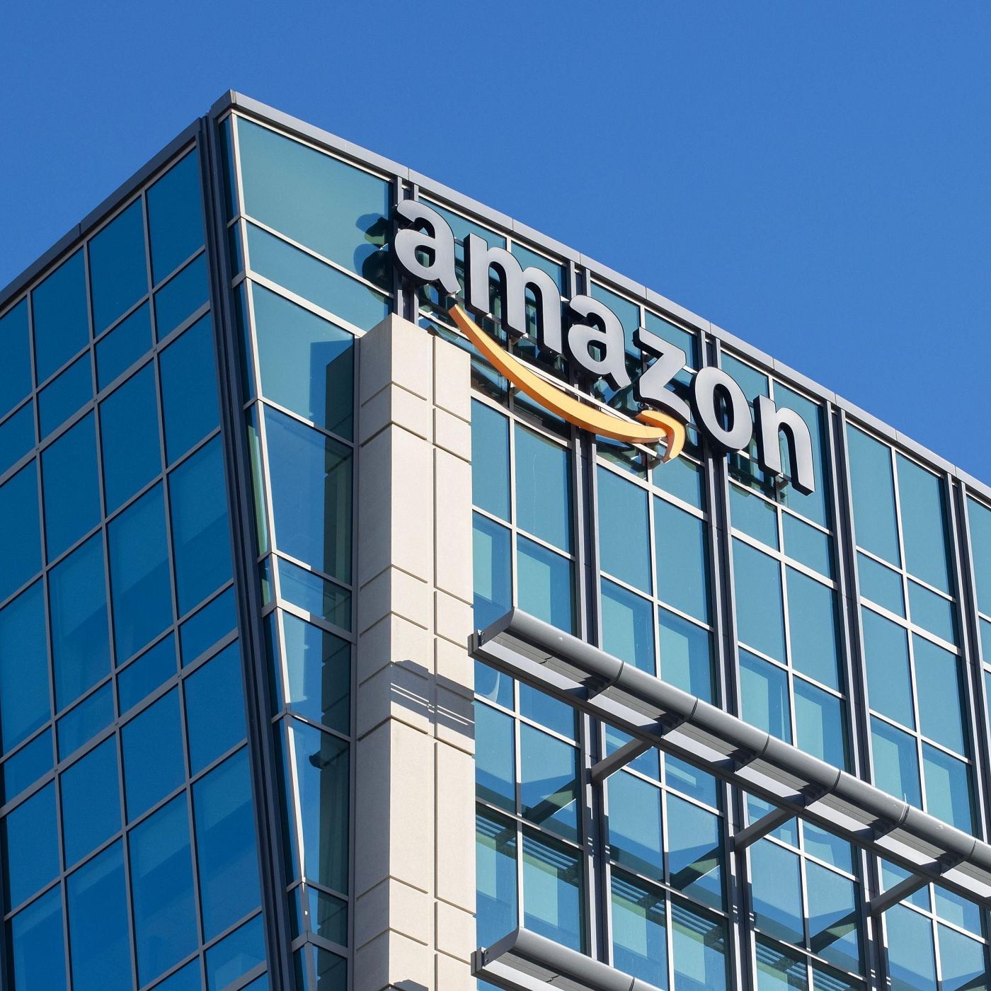 Un edificio moderno de oficinas con fachada de cristal azul y estructura de acero. En la parte superior, se aprecia el logotipo de una empresa tecnológica con una flecha naranja distintiva. El diseño incluye una sección vertical de color crema con detalles geométricos.