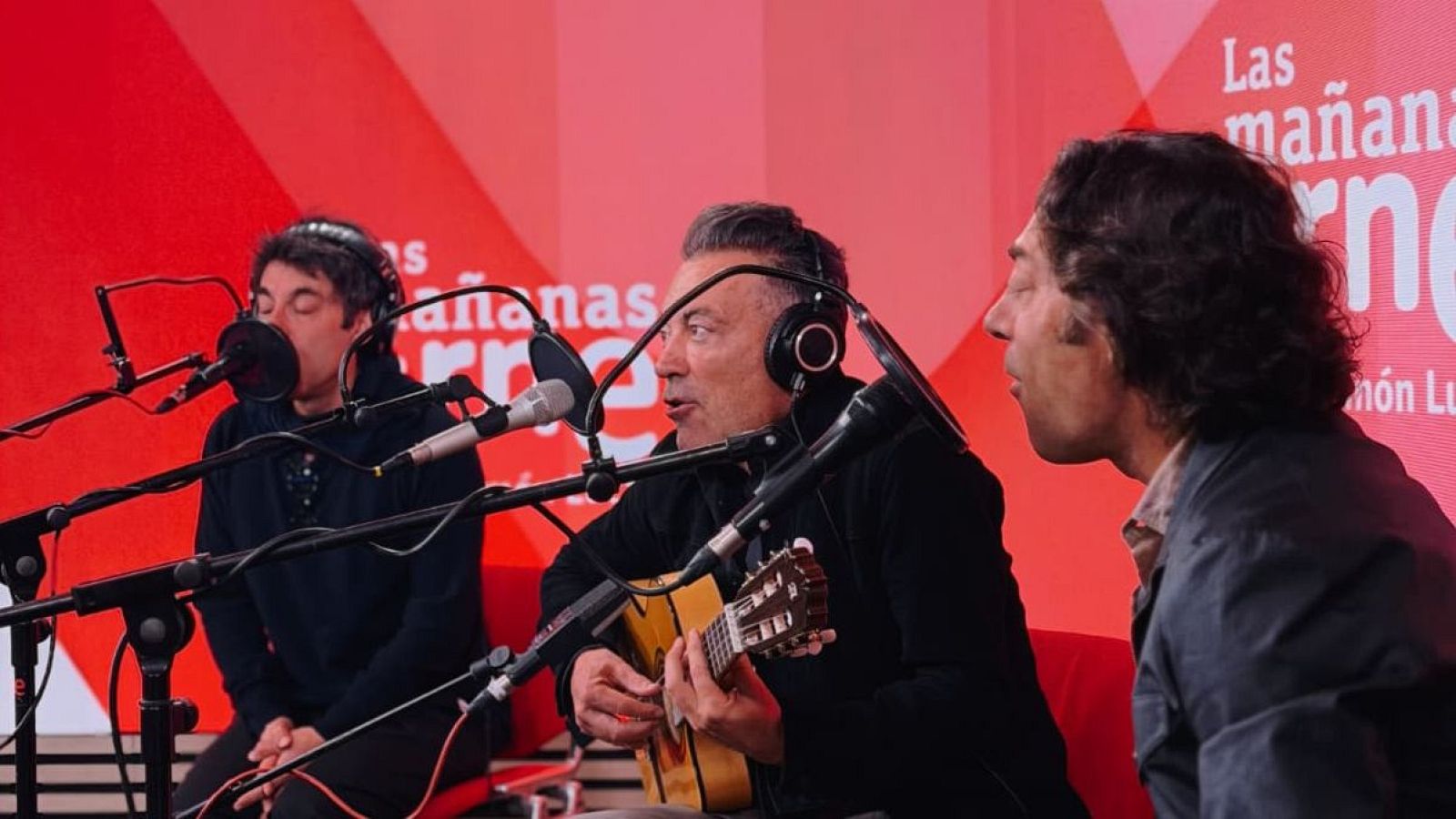 Los tres integrantes de la banda, con auriculares y micrófonos, se encuentran en un estudio de radio. Uno toca la guitarra acústica, mientras los otros dos cantan, todos vestidos con ropa oscura y clara.