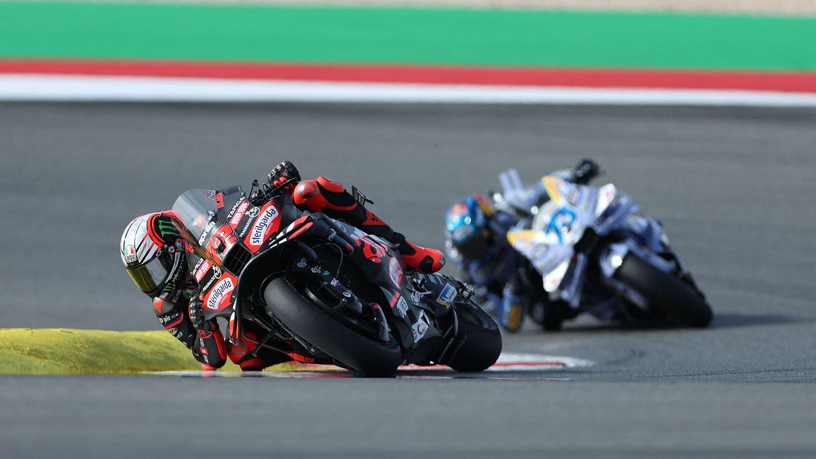 Marco Bezzecchi, con casco blanco y mono negro y rojo, compite en una carrera de MotoGP, inclinando su moto negra con detalles rojos y el patrocinador "Sterilgarda" visible.