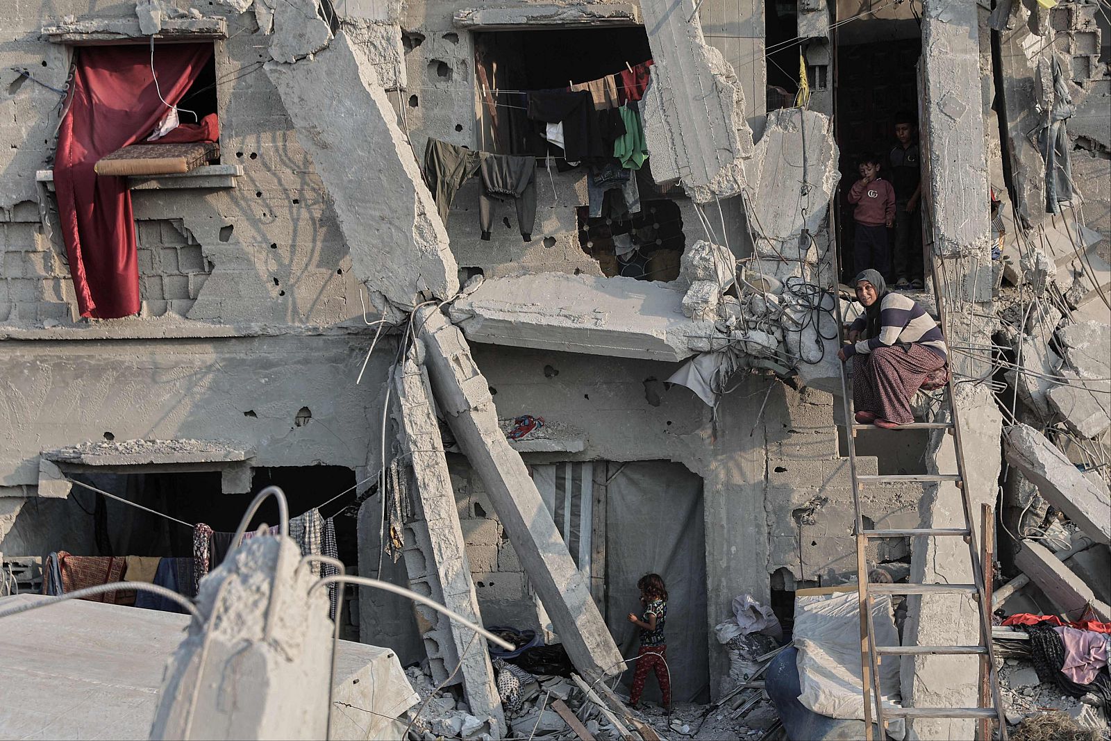 En Khan Yunis, un edificio destruido es el escenario de una escena desgarradora: una niña cerca de la base, una mujer en una escalera y dos niños en la entrada, con ropa colgada en la parte superior.