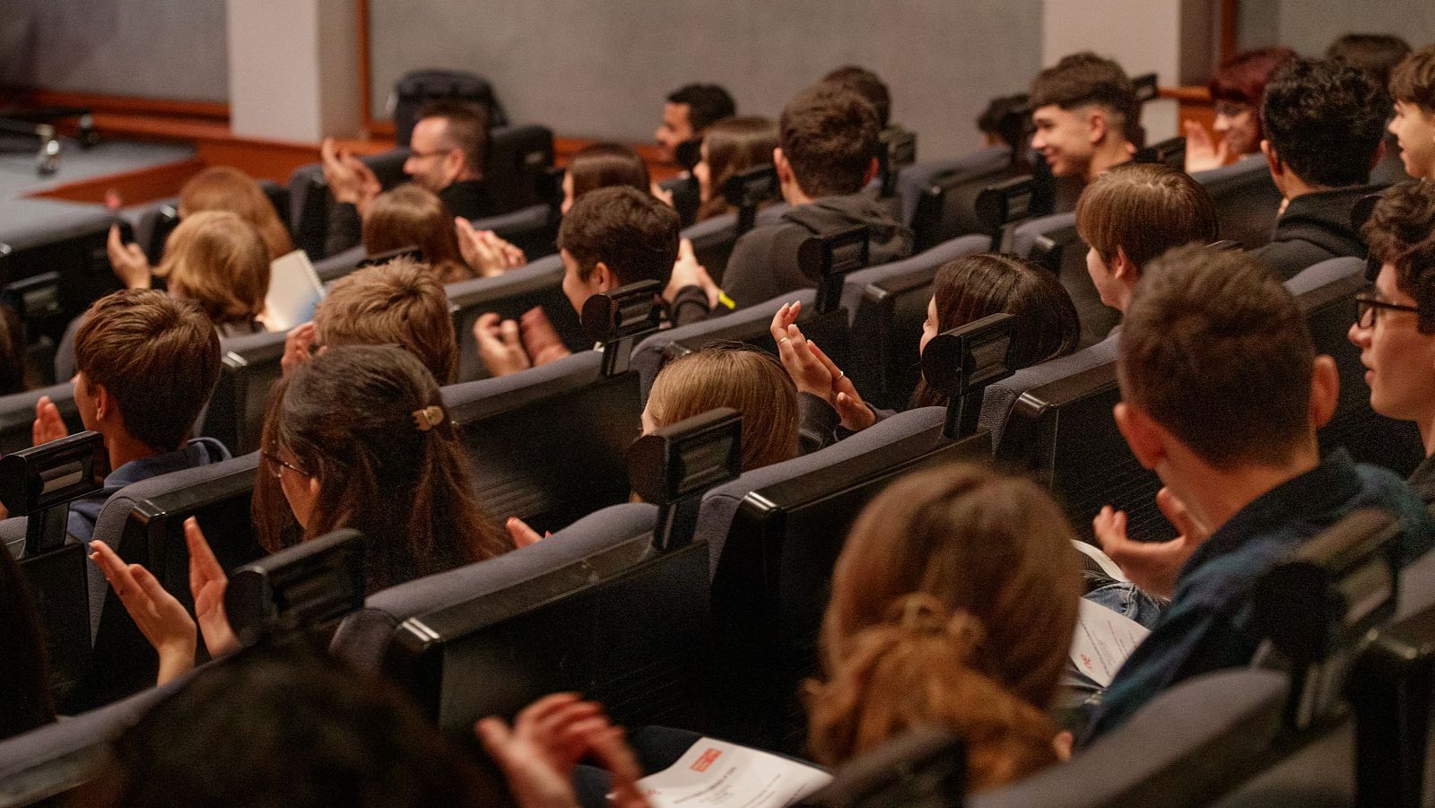 Un numeroso grupo de estudiantes de 4º de la ESO aplauden en un auditorio, posiblemente durante un evento o presentación. Se observa el texto "Chavales aplauden en 4º ESO+RTVE" y "Impulsa Visión".