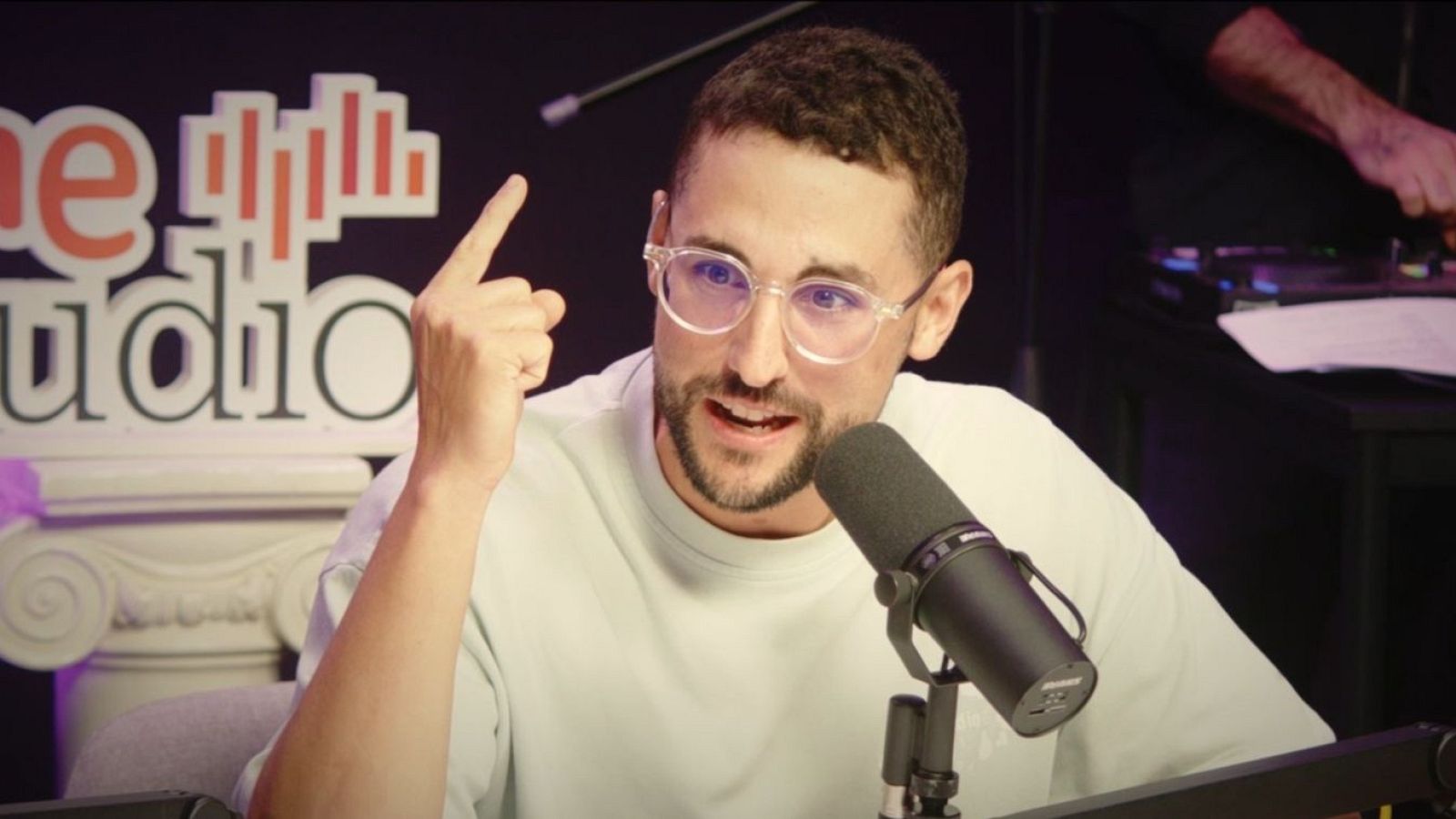 Galder Vara, con barba y gafas, está frente a un micrófono, con el dedo índice levantado. En el fondo, se observa el logo de un estudio y un tocadiscos.