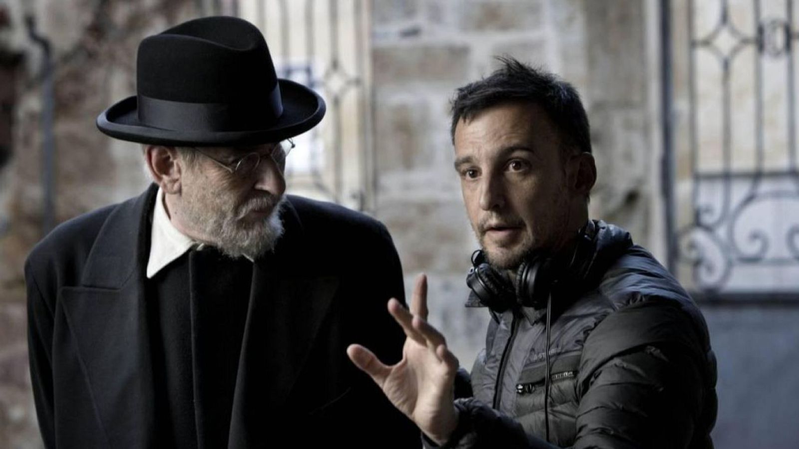 Alejandro Amenábar dirige a un hombre con sombrero y barba en un set de rodaje. El director gesticula mientras el otro hombre parece estar escuchando atentamente.