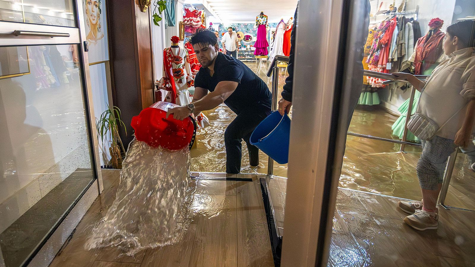 Un hombre retira el agua acumulada en el interior de un establecimiento de Huelva, a causa de las fuertes lluvias
