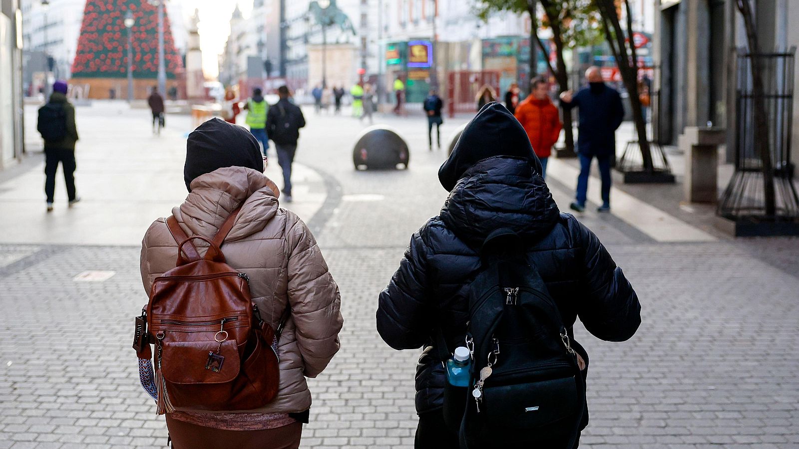 Varias personas con abrigos y gorros pasean por una calle del centro de Madrid, junto a la Puerta del Sol