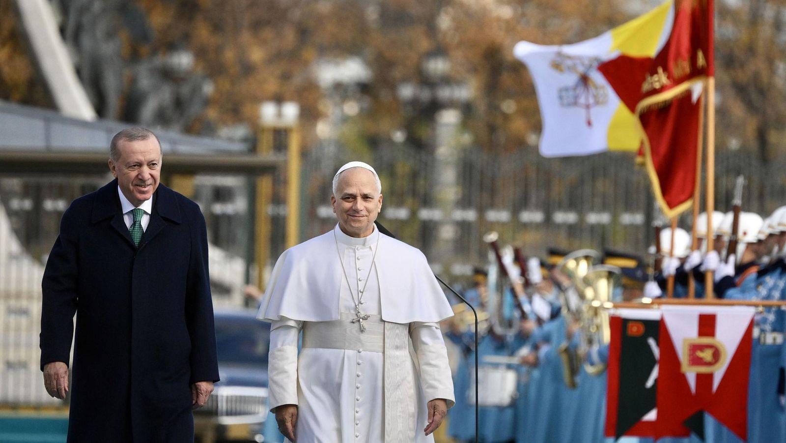 El Papa León XIV y el presidente turco, Recep Tayyip Erdogan, inspeccionan una guardia de honor durante una ceremonia en Ankara. El Papa viste de blanco y Erdogan con abrigo oscuro, mientras que la guardia porta uniformes y banderas.