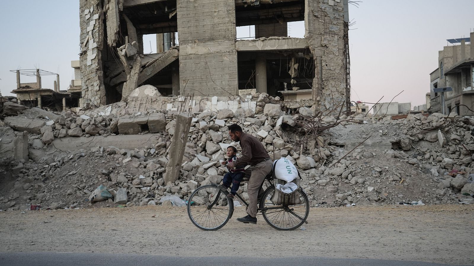 Un hombre sirio pasea en bicicleta entre edificios destruidos en Harasta.