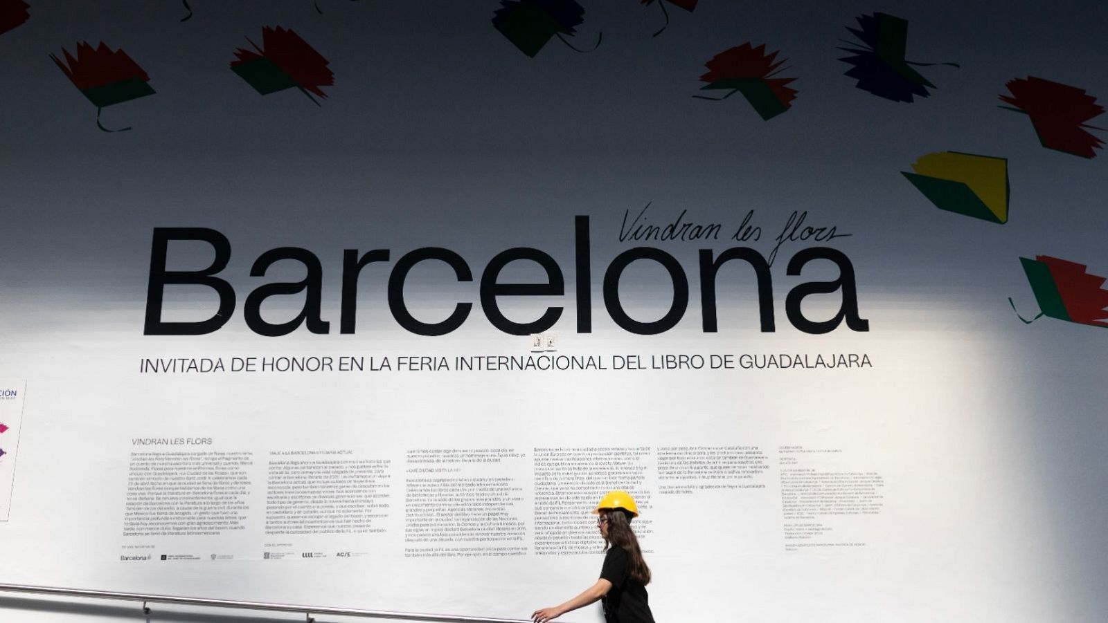 Cartell publicitari amb la paraula "Barcelona" destacada, anunciant la seva participació com a convidada d'honor en un esdeveniment literari internacional. El disseny inclou elements visuals com llibres i una persona amb casc.