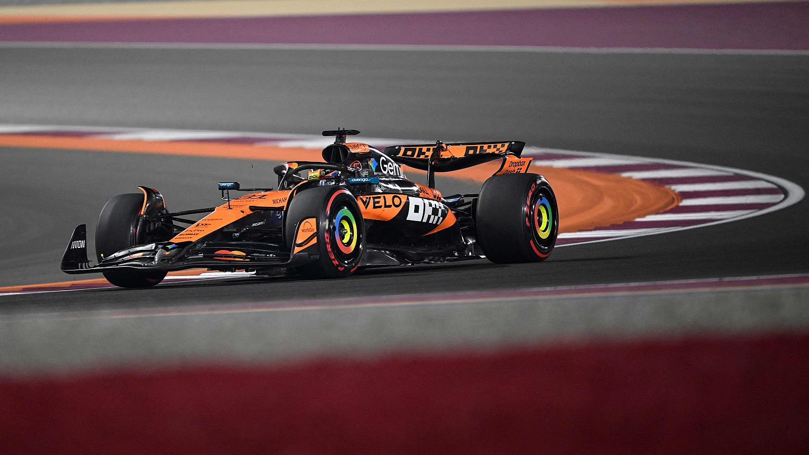 Un monoplaza de Fórmula 1, con predominio de colores naranja y negro, compite en una carrera, mostrando los logos de patrocinadores como "Velo" y "DP World" en su carrocería.