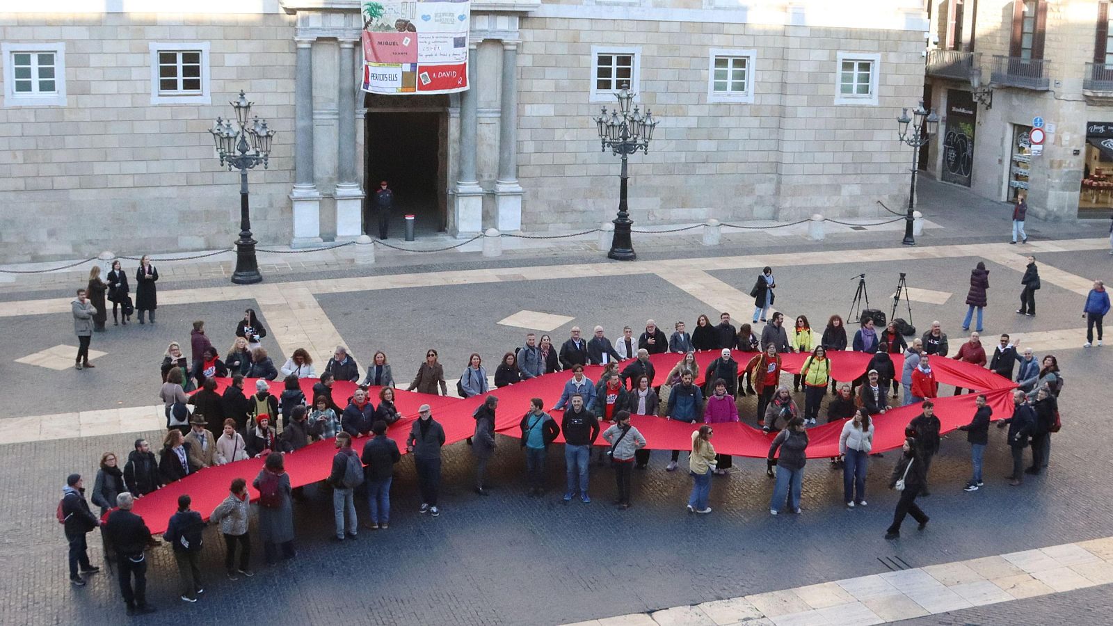 Representants d'entitats del Comitè 1r de Desembre despleguen un llaç vermell, a la plaça de Sant Jaume de Barcelona. (ACN | Laura Fíguls)