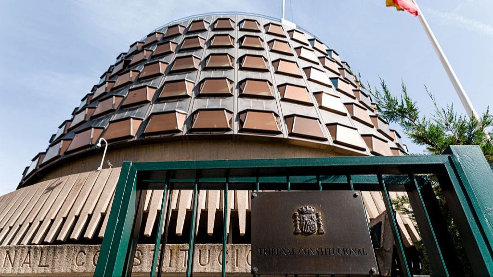 Fachada del Tribunal Constitucional español con su cúpula y bandera.  Placa identificativa en verja exterior.