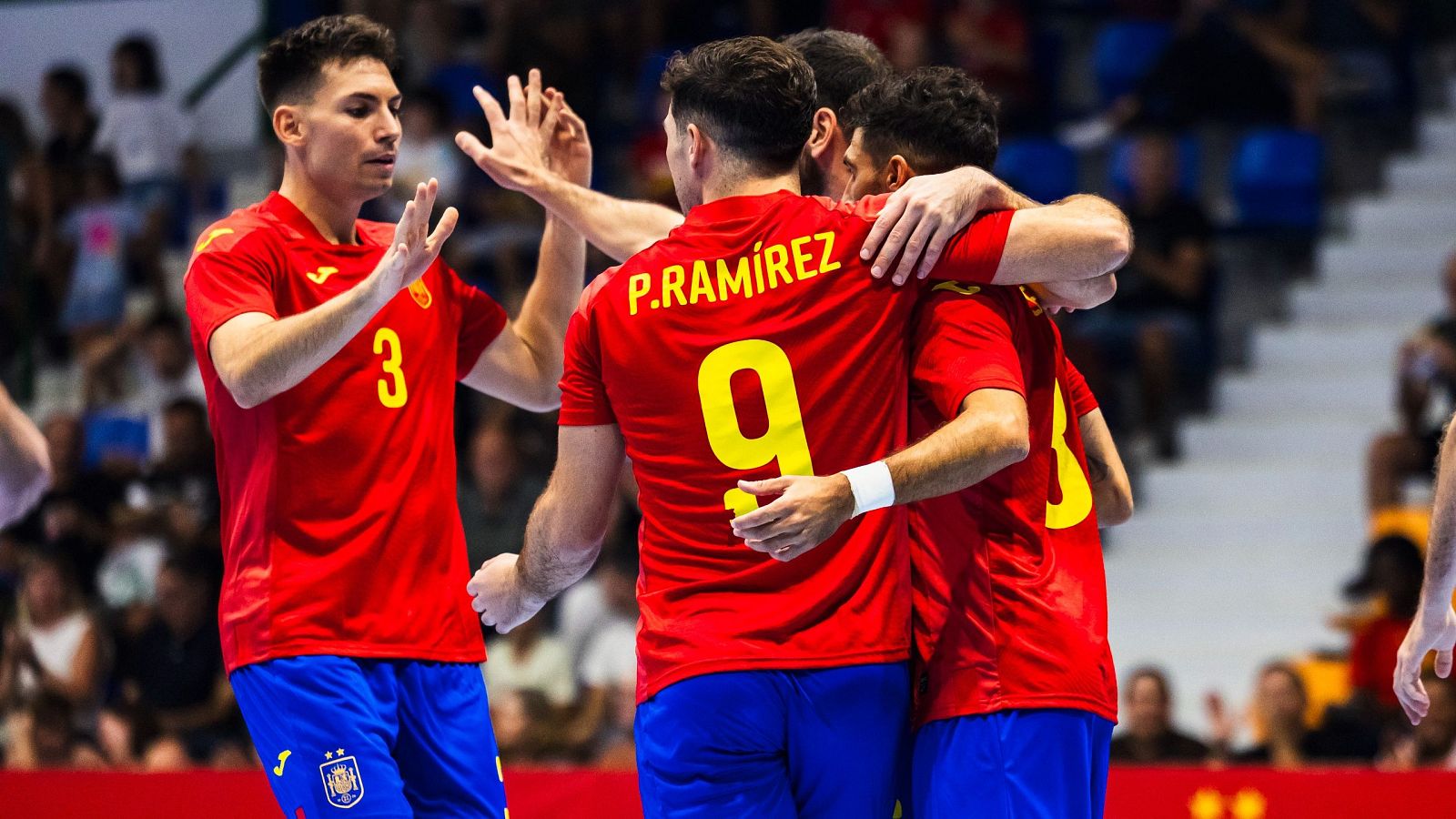 Jugadores de fútbol sala españoles celebran un gol, abrazándose y mostrando alegría. Uno lleva el dorsal 9 y el nombre "P. RAMÍREZ" en la camiseta.