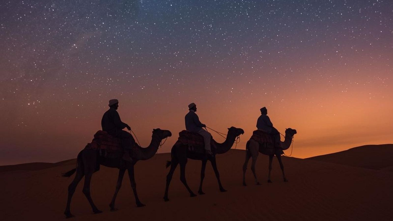 Tres siluetas montan camellos en un desierto nocturno, con un cielo estrellado y un horizonte iluminado, creando una atmósfera misteriosa.