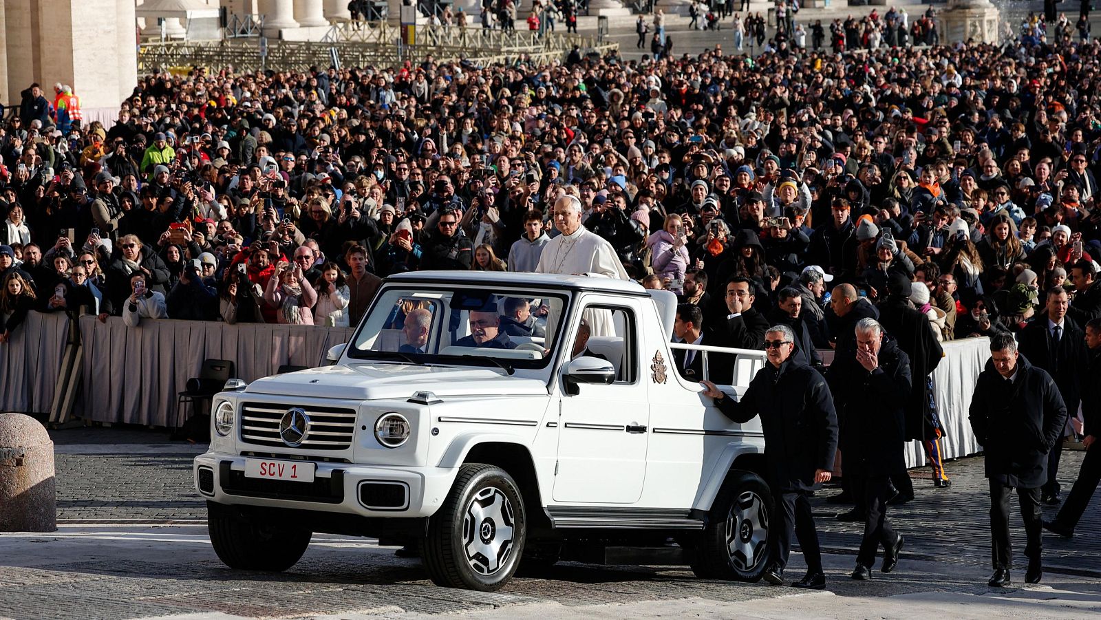El Papa León XIV, desde un vehículo descapotable, saluda a una gran multitud en la Plaza de San Pedro, con personal de seguridad alrededor y una densa concentración de personas.