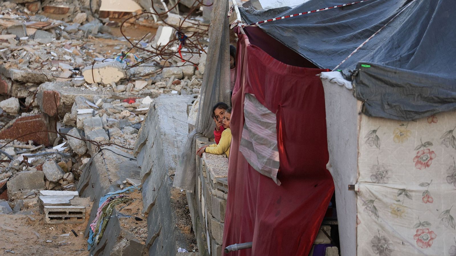 Unos niños se asoman, desde la ventana de una tienda de campaña, a los escombros de Gaza
