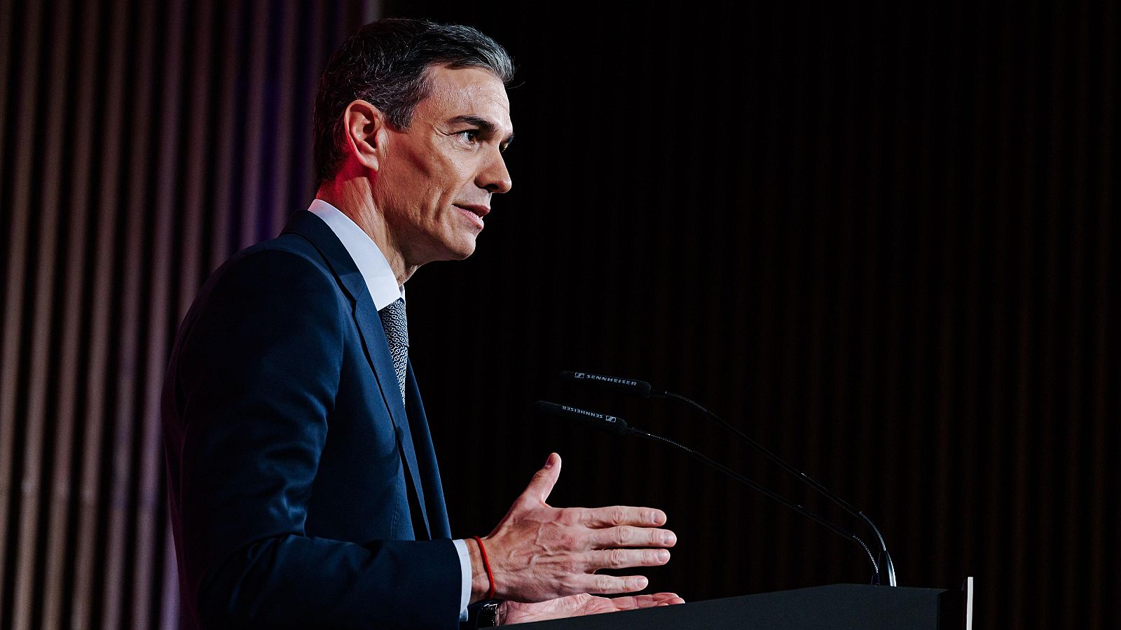 Pedro Sánchez, el presidente del Gobierno, habla desde un atril con micrófonos, vestido con traje oscuro y corbata estampada, gesticulando con la mano izquierda.