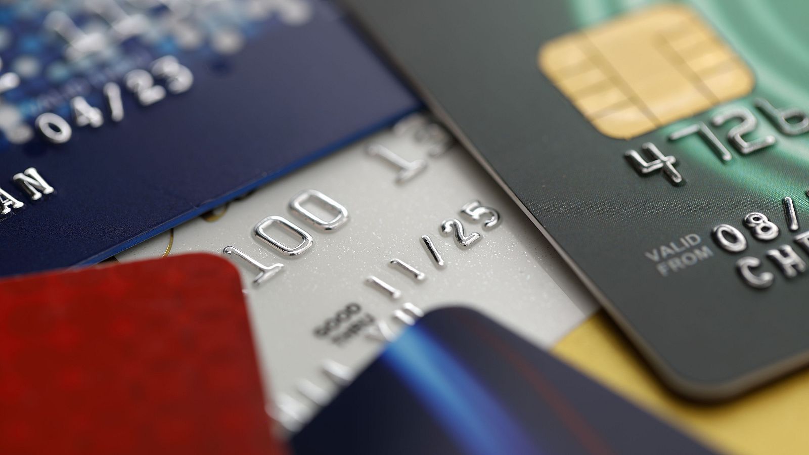 Primer plano de varias tarjetas de crédito superpuestas, mostrando detalles como fechas de vencimiento y números parciales. Se aprecian tarjetas de diferentes colores, incluyendo azul, plateado, verde oscuro y rojo.